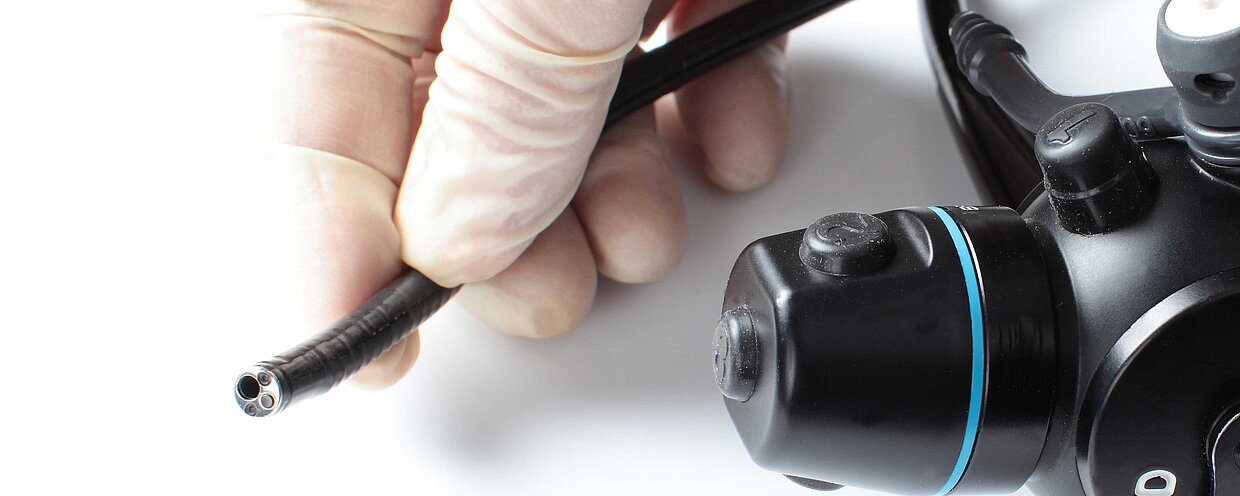 A hand wearing a surgical glove holds an endoscope.