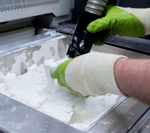 Blick von der Seite auf eine Reinigungssituation, in der 2 Hände ein 3D-Druck-Bauteil durch Absaugung reinigen