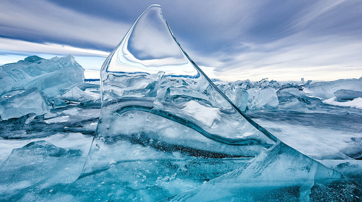 Eisformationen auf einem gefrorenen See Eisformationen auf einem gefrorenen See unter einem dramatischen Himmel, mit klaren, blauen Eisstrukturen im Vordergrund