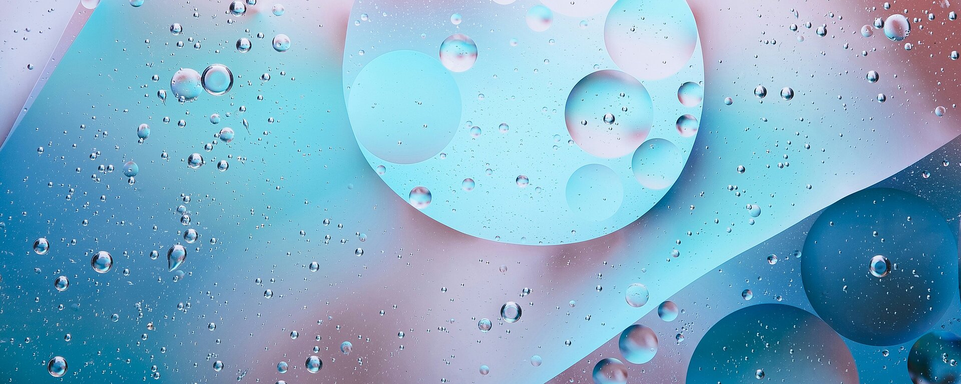 Abstrakte Darstellung von schwebenden Öl- und Wasserblasen in sanften Blau- und Rosatönen, die ein faszinierendes Muster auf hellem Hintergrund bilden