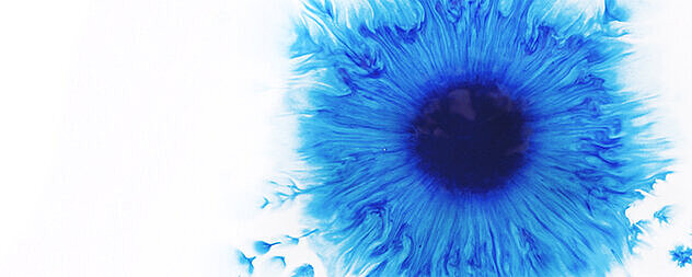 Ein zerfliessender, blauer Farbklecks auf Aquarellpapier 
