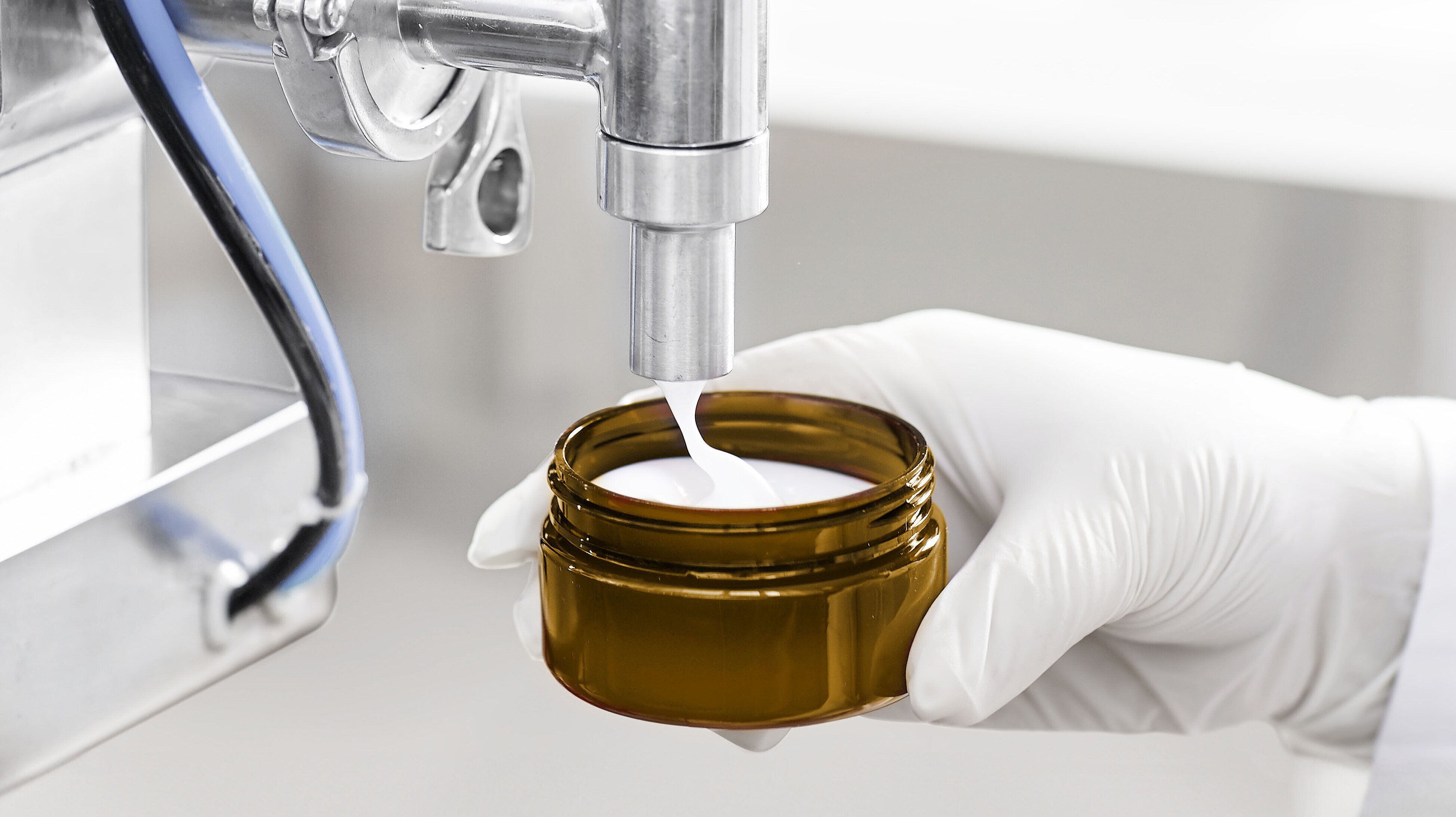 Industrielle Abfüllmaschine, die Creme in ein braunes Glasgefäß füllt.