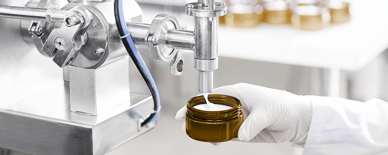 Industrielle Abfüllmaschine, die Creme in ein braunes Glasgefäß füllt.