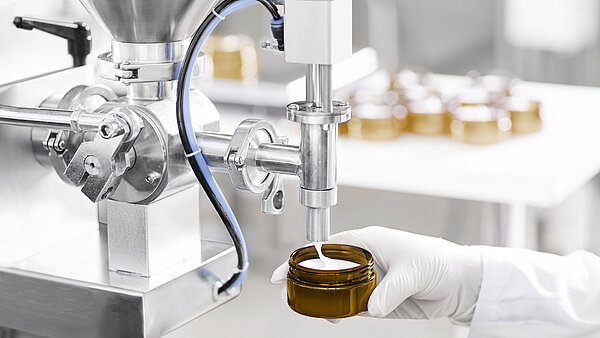 Industrielle Abfüllmaschine, die Creme in ein braunes Glasgefäß füllt.