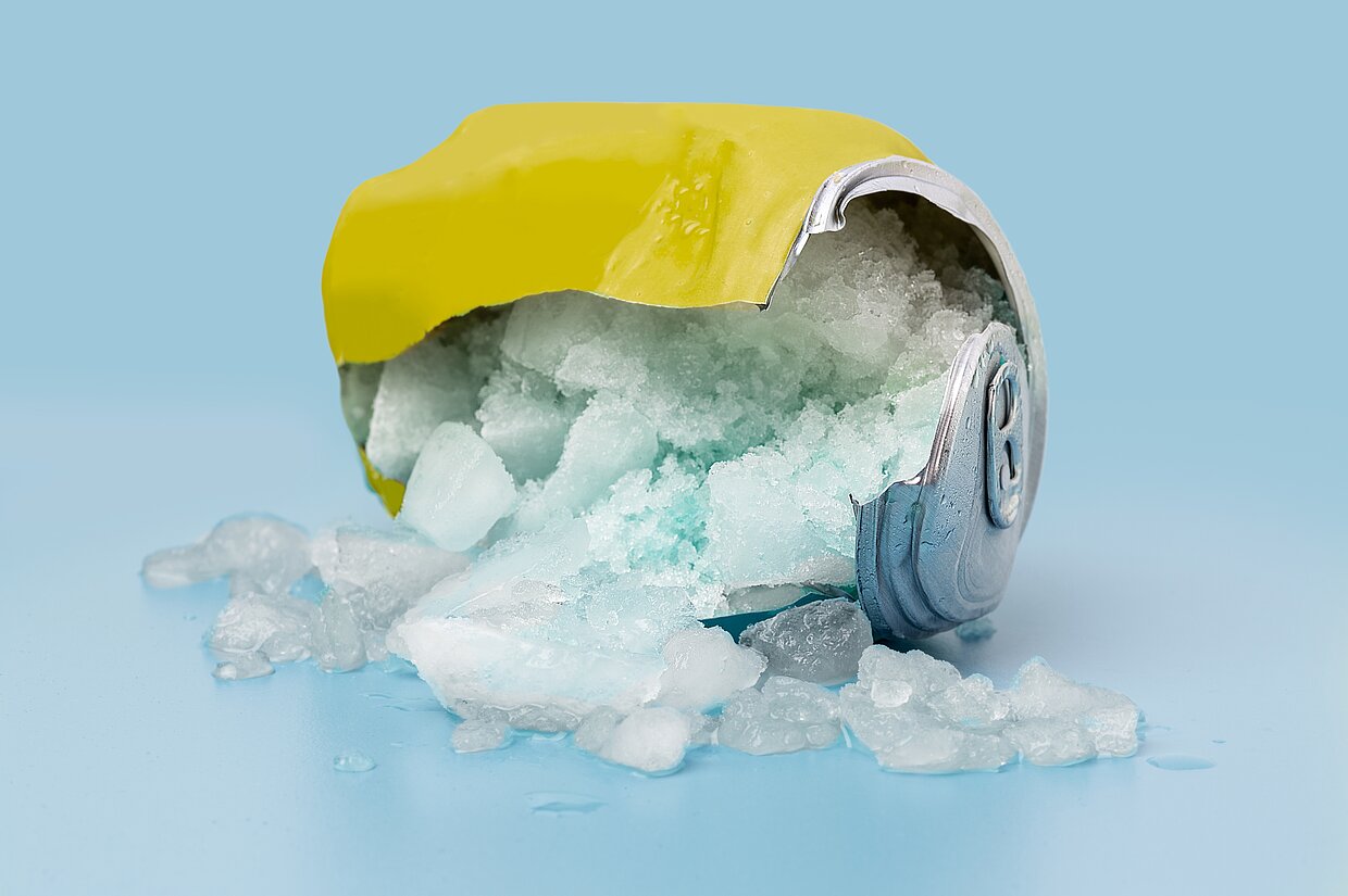 Zerdrückte Getränkedose mit gefrorenem Inhalt Zerdrückte Getränkedose mit gefrorenem Inhalt, die auf einer blauen Oberfläche liegt, mit Eisstücken, die aus der Dose herausquellen