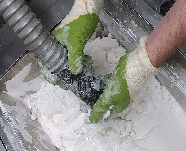 Blick von oben auf ein mit Reinigungsbecken, in dem 2 Hände ein 3D-Druck-Bauteil durch Absaugung reinigen