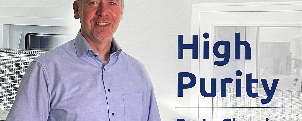 Armand Oostendoop, Geschäftsführer mafac, in einem hellblauen Hemd vor einem Hintergrund mit dem MAFAC-Logo und dem Text ‘High Purity Parts Cleaning, water-based & solvent-free’