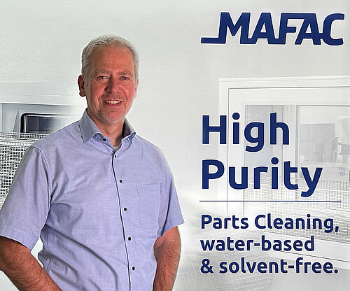 Armand Oostendoop, Geschäftsführer mafac Armand Oostendoop, Geschäftsführer mafac, in einem hellblauen Hemd vor einem Hintergrund mit dem MAFAC-Logo und dem Text ‘High Purity Parts Cleaning, water-based & solvent-free’
