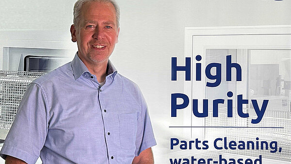 Armand Oostendoop, Geschäftsführer mafac, in einem hellblauen Hemd vor einem Hintergrund mit dem MAFAC-Logo und dem Text ‘High Purity Parts Cleaning, water-based & solvent-free’