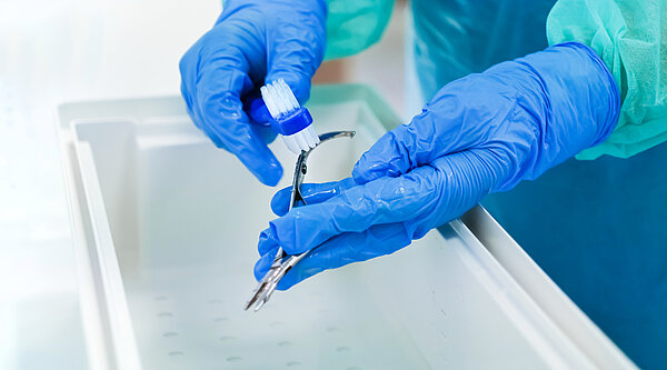 Zwei Hände in OP-Handschuhen reinigen mit Bürste Operations-werkzeug